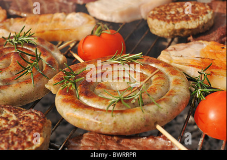 Spirale Cumberland Würstchen und Sonstiges Fleisch im Freien auf einem Holzkohlegrill gegrillt. Stockfoto