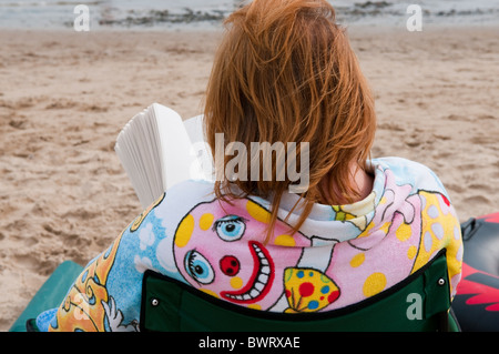 eine Frau eingewickelt in ein Handtuch, ein Buch am Strand lesen Stockfoto