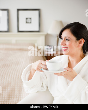 Hispanic Frau im Bademantel Kaffeetrinken im Schlafzimmer Stockfoto