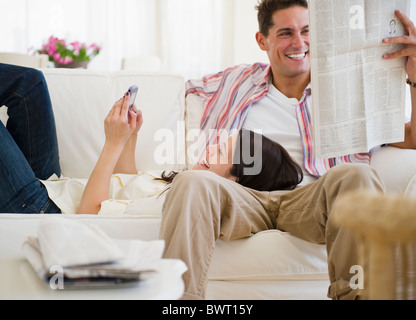 Lächeln, paar gemütlich auf Sofa zusammen mit Handy und Zeitung Stockfoto