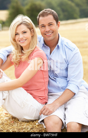 Paar sitzt auf Strohballen In abgeernteten Feld Stockfoto