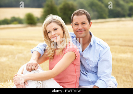 Paar sitzt auf Strohballen In abgeernteten Feld Stockfoto