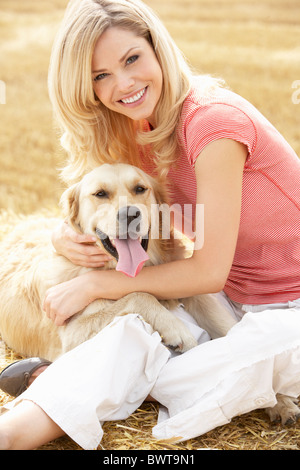 Frau mit Hund auf Strohballen In abgeernteten Feld Stockfoto