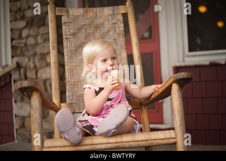 kleine blonde Mädchen isst Eis in einem großen Schaukelstuhl Stockfoto