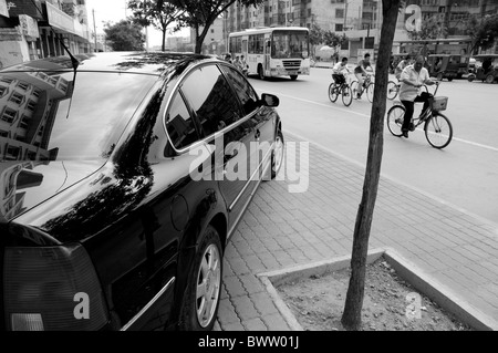 Schwarzes Auto geparkt auf dem Bürgersteig Menschen auf Fahrrädern vorbei, Datong, Shanxi, China fahren. Stockfoto