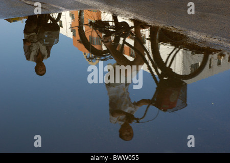 Reflexion von zwei Menschen auf Fahrrädern in einer Pfütze auf der Straße, Datong, Shanxi, China. Stockfoto