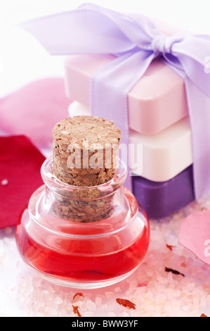 Badeöl in einem Kolben mit Rosenblättern, Badesalz und Seife im Hintergrund Stockfoto