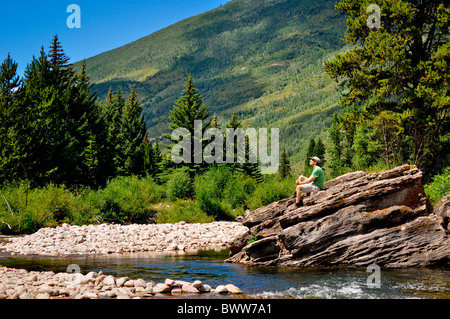 Mann sitzt auf einem großen Felsen am creekside Stockfoto