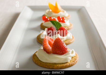 Kekse mit cremiger Käse verteilen, garniert mit Himbeeren, Minze, Erdbeeren, rote Johannisbeere und gelben Pflaumen oben auf einen whi Stockfoto