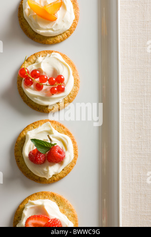 Kekse mit cremiger Käse verteilen, garniert mit Himbeeren, Minze, Erdbeeren, rote Johannisbeere und gelben Pflaumen oben auf einen whi Stockfoto