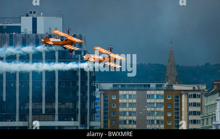 Zwei Paar von Breitling Boeing Stearman Doppeldecker in Eastbourne Airbourne Air Display mit einem Wingwalkers vorbeifliegen Stadtgebäude Stockfoto