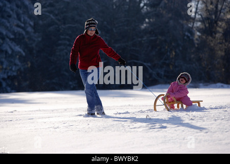 Frau Kleinkind Mädchen auf Holzschlitten in Winterlandschaft, Dobel, Schwarzwald, Gerrmany ziehen Stockfoto