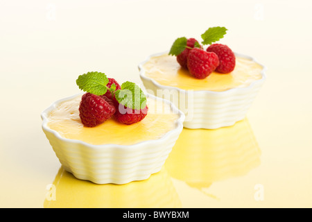 zwei Schüsseln mit Vanille Pudding, garniert mit Himbeeren auf reflektierende helle gelbe Oberfläche, selektiven Fokus Stockfoto