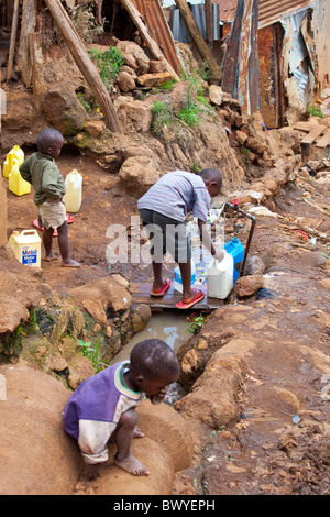 Jungen Behälter einfüllen von Wasser aus einem Hahn in den Kibera Slums, Nairobi, Kenia Stockfoto