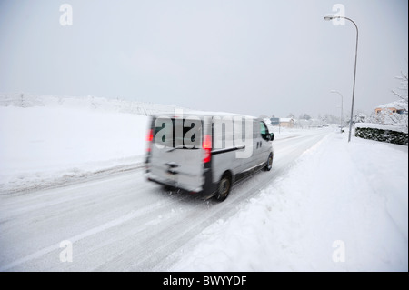 Ein weißer Lieferwagen fährt auf einer verschneiten Straße in einer Schweizer Stadt. Bewegungsunschärfe auf dem Wagen. Stockfoto