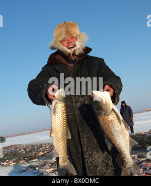 Lächelnde Fischer hält zwei große Fische im Winter Angeln, Dorbod mongolische autonome Grafschaft, Heilongjiang, China Stockfoto