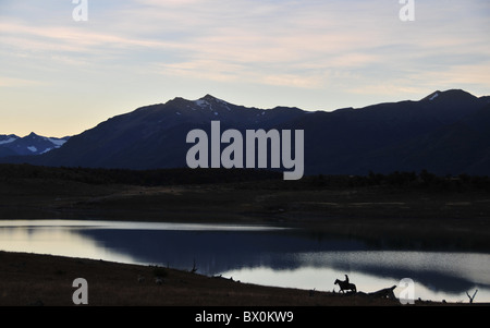 Sonnenuntergang Silhouette der Andengipfel und Pferd Gaucho reflektiert in den stillen Wassern des Lago Roca, Anden, Patagonien, Argentinien Stockfoto