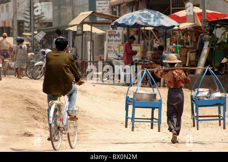 Ein Lebensmittel-Verkäufer, die zu Fuß ist und ein Mann mit dem Fahrrad Teile eine staubigen Schmutz Straße in Myawaddy, Birma (Myanmar). Stockfoto