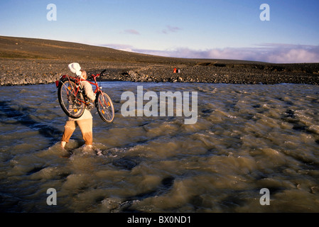 Mann mit dem Fahrrad auf der Schulter, die Überquerung eines Flusses, Island. Stockfoto