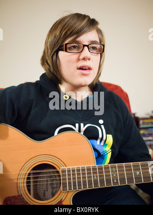 Ein junges Mädchen, das Tragen der Brille eine 12-saitige akustische Gitarre spielen und singen. Stockfoto