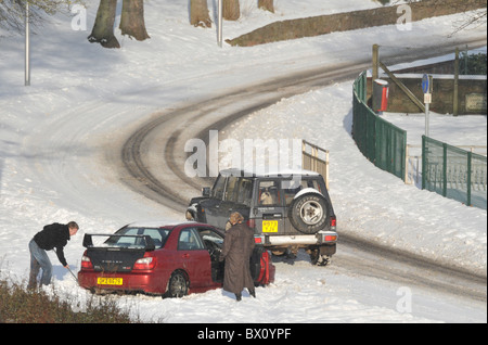 ein junger Mann löscht den Schnee unter die Reifen seines Wagens gefangen im Schnee. Stockfoto