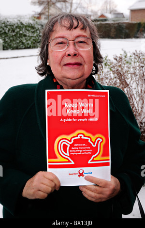 74 Jahre alte Frau Dame Rentner halten HM Regierung Faltblatt halten Sie WARM zu halten gut mit Bild von Teekanne und Beratung Stockfoto