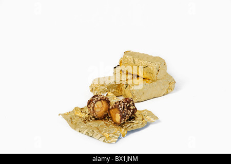 Eine offene Stück Schokolade Almond Roca ist vor einige gestapelte Stücke in ihren Goldfolie Wrapper angezeigt. Stockfoto