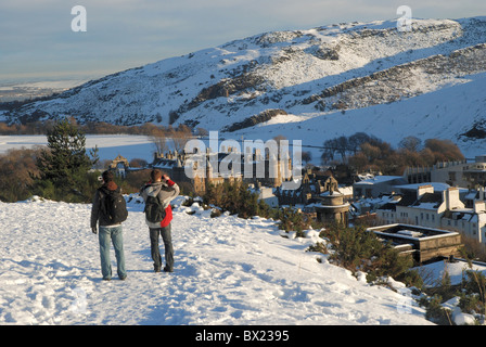 Zwei Touristen zu Fuß auf einem verschneiten Calton Hill in Edinburgh und den Blick in Richtung Holyrood Palace zu fotografieren. Stockfoto