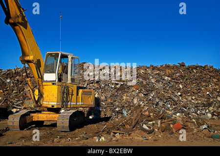 Ein großer gelber Kran arbeitet mit ein riesiger Haufen Schrott, immer bereit für das recycling unter strahlend blauem Himmel. Stockfoto
