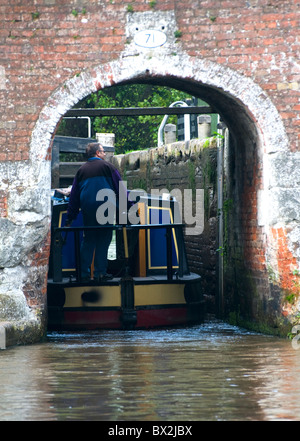 Lenkung Narrowboat-Kanal Boot /barge in Schloss unter viktorianischen Backsteinbogen Mann. Porträt-Größe Stockfoto