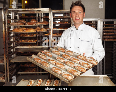 Porträt eines Bäckers hält ein Tablett mit frisch gebackenen Brötchen in einer Bäckerei Stockfoto