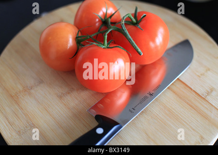 Rote Tomaten und ein Stahl Messer auf Schneidebrett Stockfoto