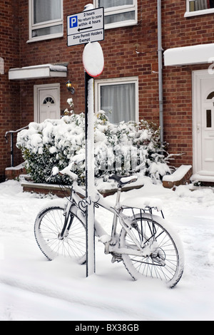 Schnee bedeckte Fahrrad angekettet an einen Pfosten Stockfoto