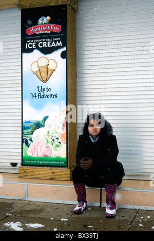 Frau sitzt außerhalb geschlossener Eisdiele im Schneesturm Stockfoto