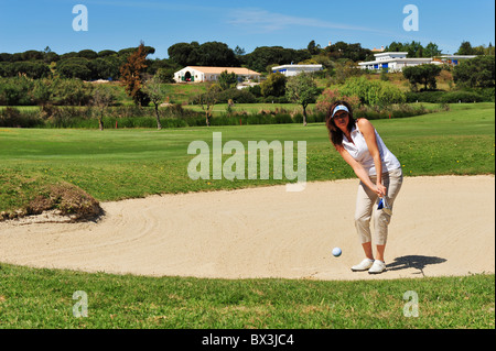 Junge Dame Golfer tragen eine Sonnenblende, ihr Gesicht zu schattieren, während ein Schuss aus dem Sandfang Bunker spielen. Stockfoto