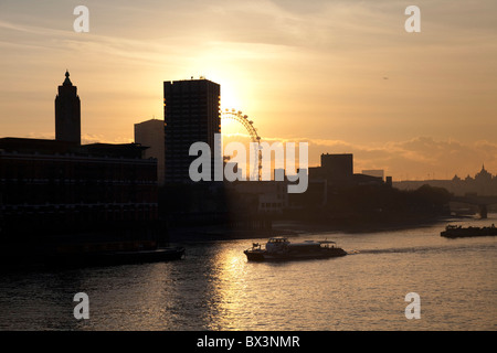 Sonnenuntergang hinter einem hohen Gebäude, Blick über den Fluss Themse als Boote auf die Skyline von Southbank vorbei. Stockfoto