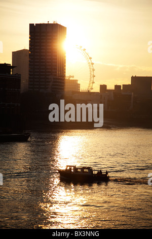 Sonnenuntergang hinter einem hohen Gebäude, Blick über den Fluss Themse als Boote auf die Skyline von Southbank vorbei. Stockfoto