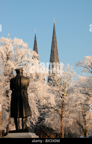 Bronzestatue von Captain Smith von der Titanic, mit Blick auf die Türme der Kathedrale von Lichfield im Winter mit Raureif auf Bäumen Stockfoto