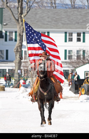 Ein Pferd und Cowboy trägt die USA-Flagge, amerikanische Flagge, während der Beginn der Veranstaltung Skijöring. Stockfoto