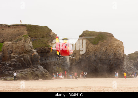 Flugrettung schwebt über einem Strand in Hayle Cornwall nach einer Person ist von der Klippe zum Strand gefallen. Stockfoto