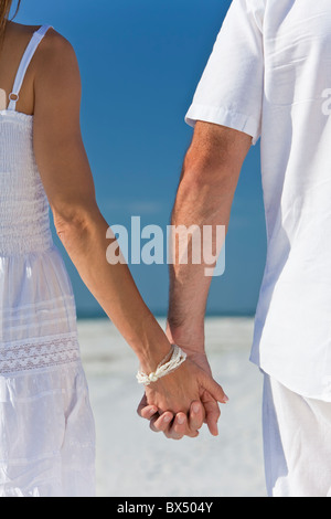 Rückansicht von Mann und Frau romantisch zu zweit in weißen Kleidern Hand in Hand und zu Fuß auf einem einsamen tropischen Strand Stockfoto