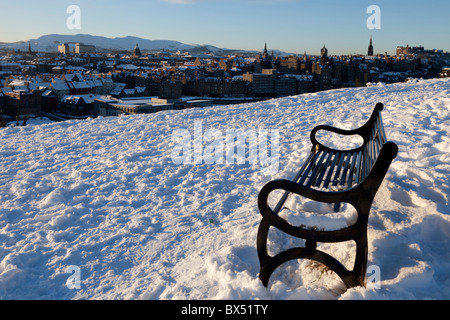 Leere Bank in frühen Morgensonne auf einem verschneiten Calton Hill, Blick über Edinburgh, Scotland, UK Stockfoto