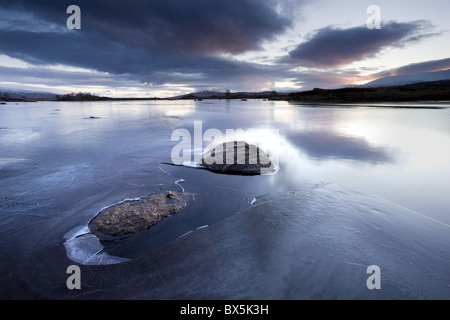 Winter-Blick auf Loch Ba "im Morgengrauen, Loch teilweise gefroren mit zwei großen Felsen ragen aus dem Iceg, Rannoch Moo, Scotland, UK Stockfoto