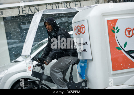 Ein Mann fährt ein Fahrrad betrieben Post und Paket Lieferwagen im Schnee in Paris, Frankreich. Stockfoto