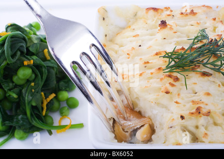 Lachs und Schellfisch Fisch pie, mit einer Gabel tauchen in für ein Stück. schönes Erbsen und Spinat Salat als Beilage. Stockfoto