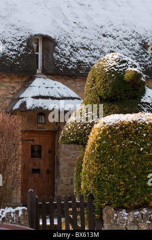 Ein malerisches Reetdachhaus im Winterschnee mit Vogel geformte Hecke. Chipping Campden in Cotswolds. Gloucestershire. England Stockfoto