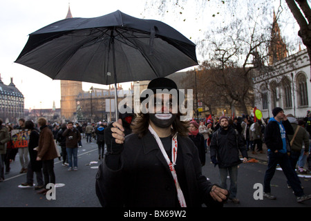 Ein Mann mit Clown Make-up und Regenschirm protestieren gegen Aufstieg zu Studiengebühren im Zentrum von London. Stockfoto