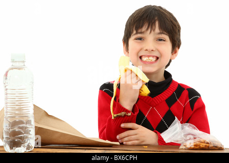 Attraktive 7 jährige französische amerikanischen junge in Schulbank über weiße ein Lunchpaket oder einen Snack zu essen. Stockfoto