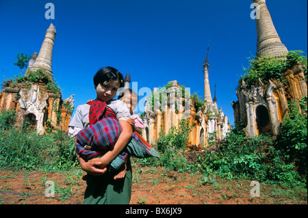 Junges Mädchen mit Baby auf dem Rücken vor alten Stupas in Indein archäologischen Stätte, Inle-See, Myanmar (Burma) Stockfoto