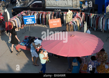 Frauen Shopper befinden sich Einkaufsmöglichkeiten für Kleidung zu einem Straßenmarkt mit einem großen Sonnenschirm in Nan, Thailand. Stockfoto